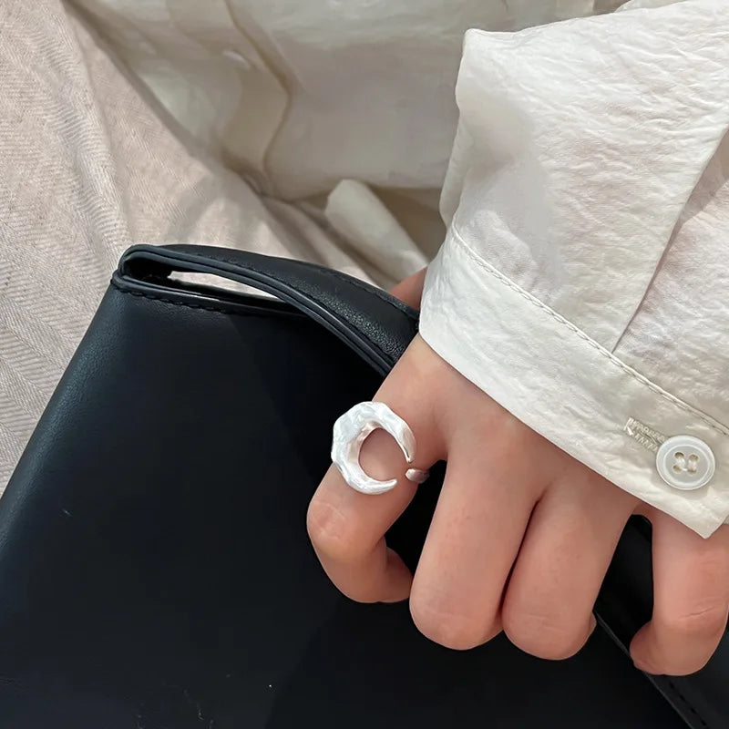 Hand wearing a silver moon ring on a black surface with a blurred background