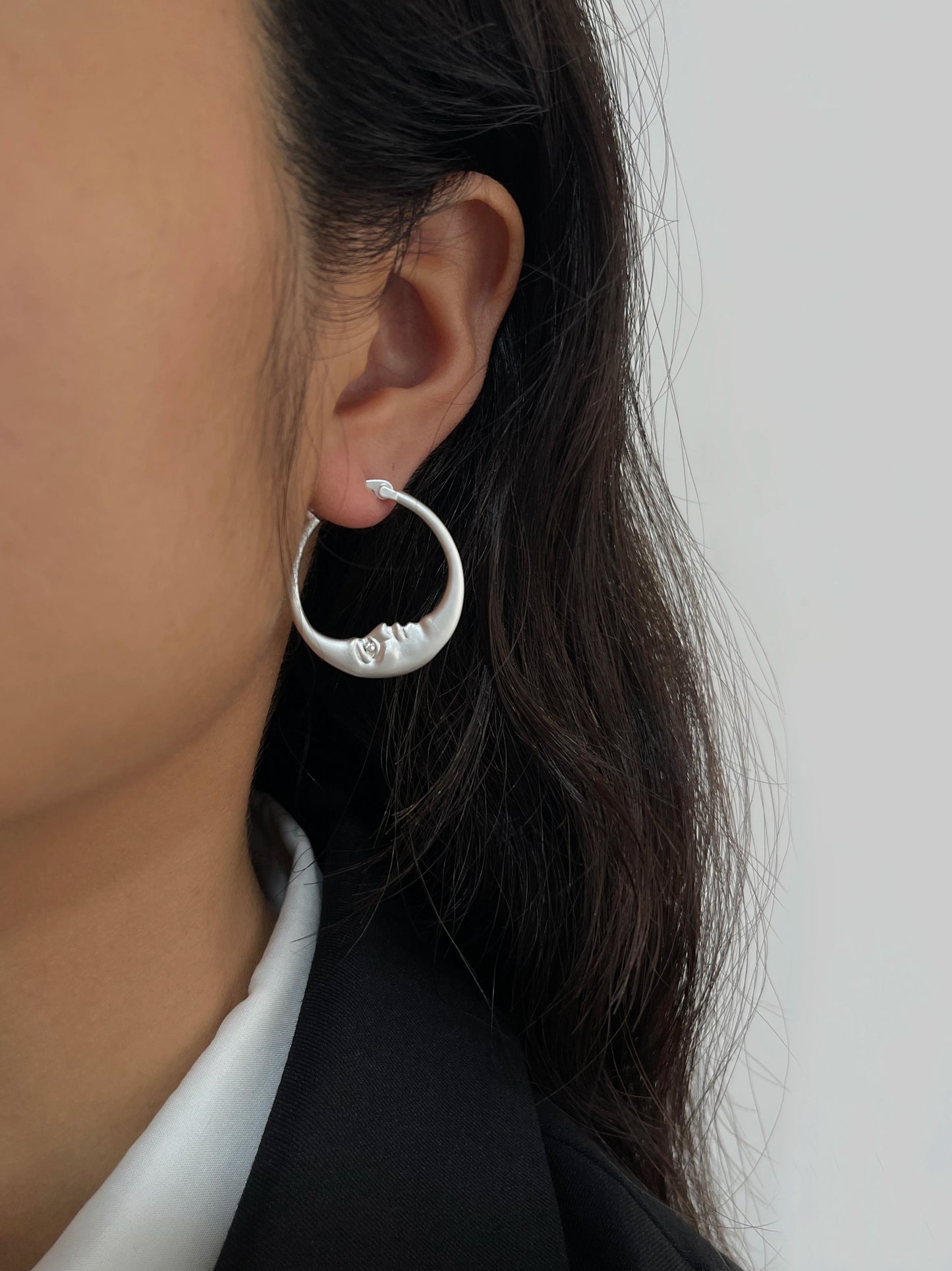 Close-up of a person wearing a silver hoop earring with a small round pendant on a plain background