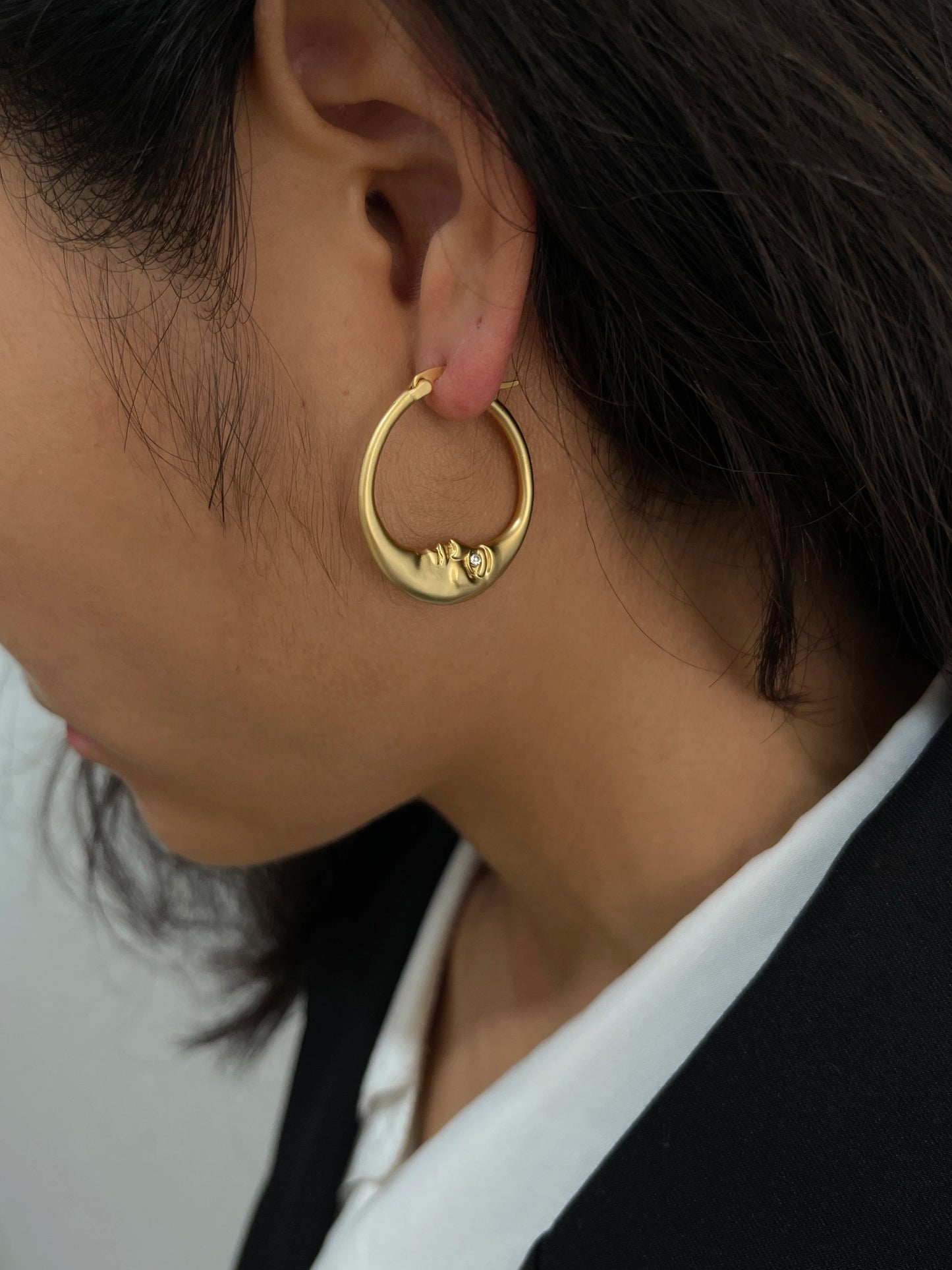 Gold hoop earring worn by a person with dark hair.