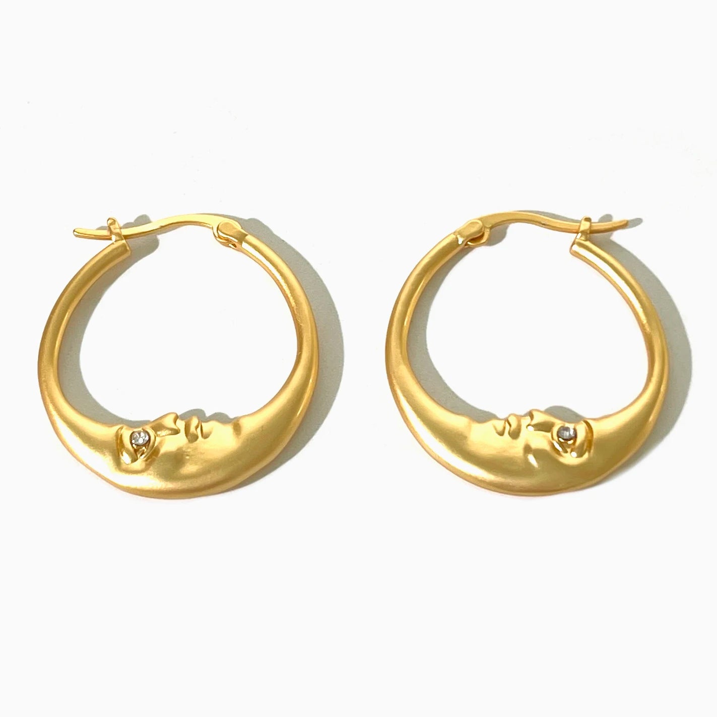 Gold hoop earrings with face designs on a white background
