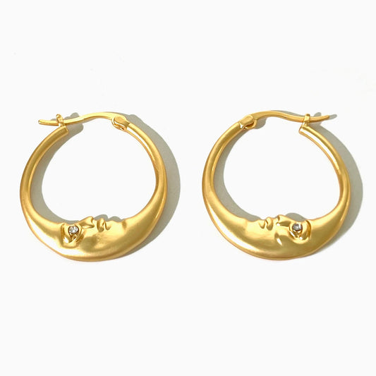 Gold hoop earrings with face designs on a white background