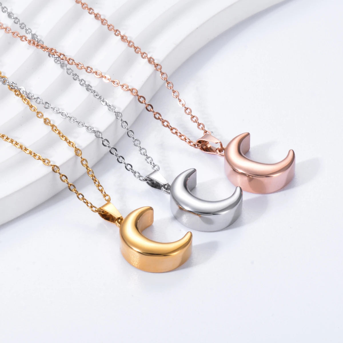 Three moon-shaped pendants on chains against a white background