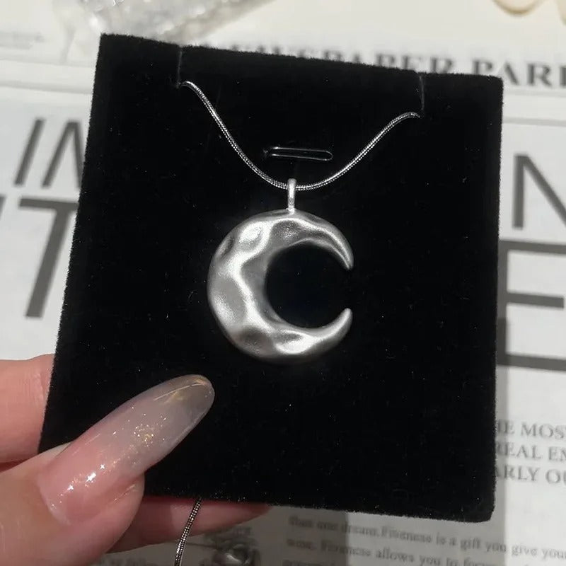 Silver crescent moon necklace on a black velvet display card.