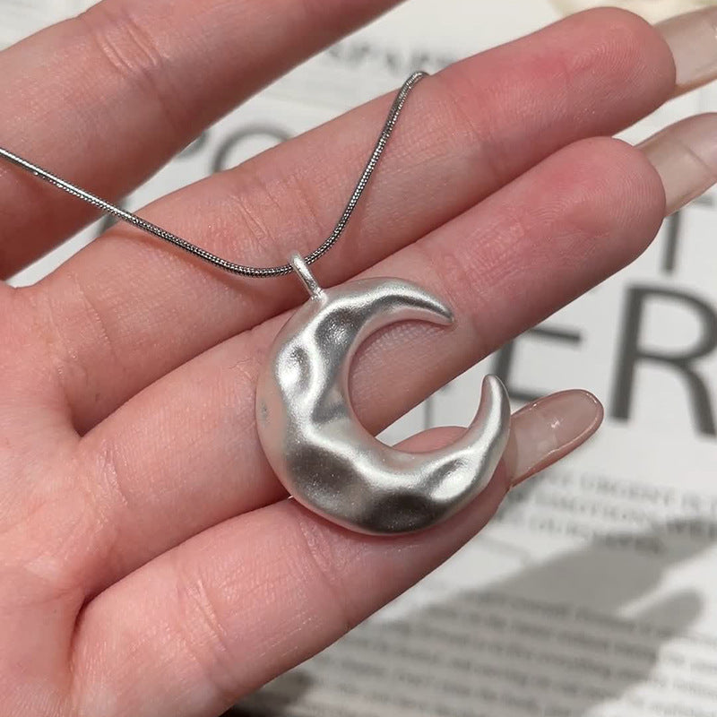 Silver crescent moon pendant on a chain held in a hand with a blurred newspaper background