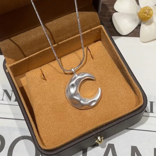 Silver crescent moon necklace in a jewelry box with a white flower in the background