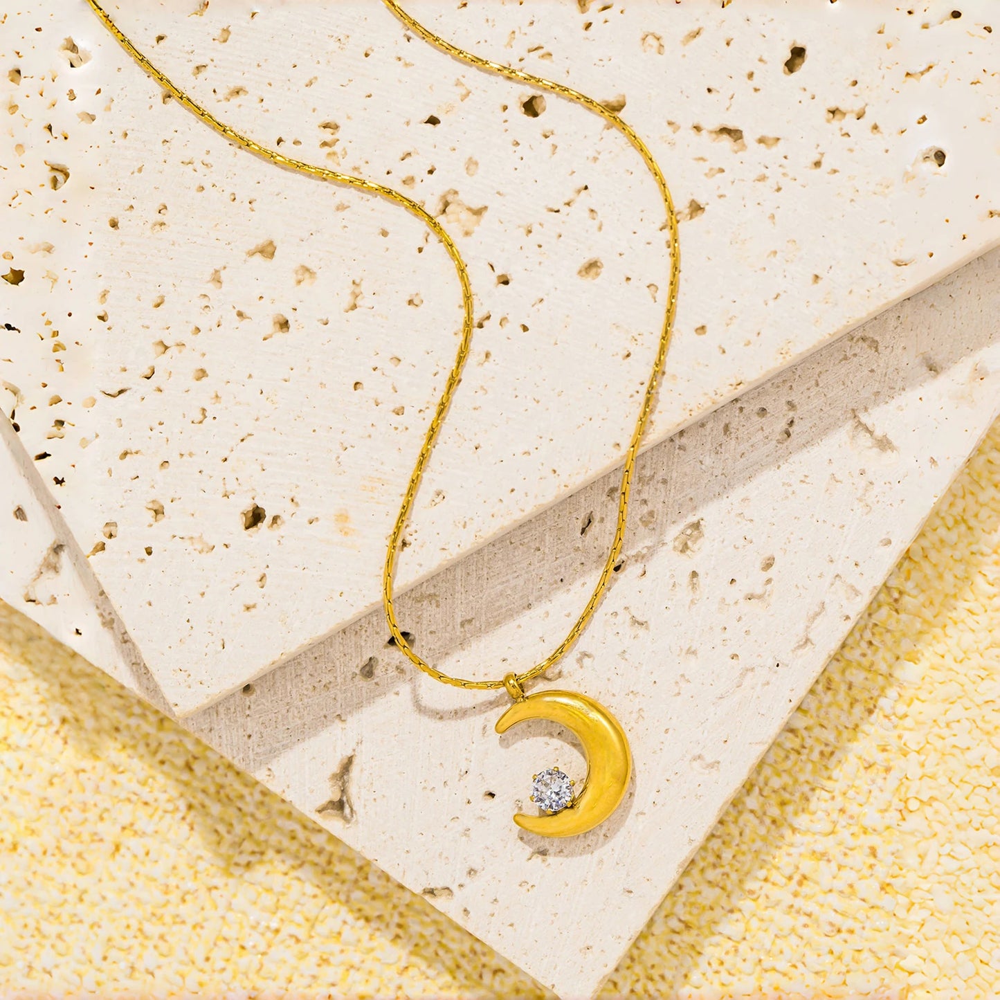 Gold necklace with a crescent moon pendant on a textured beige surface