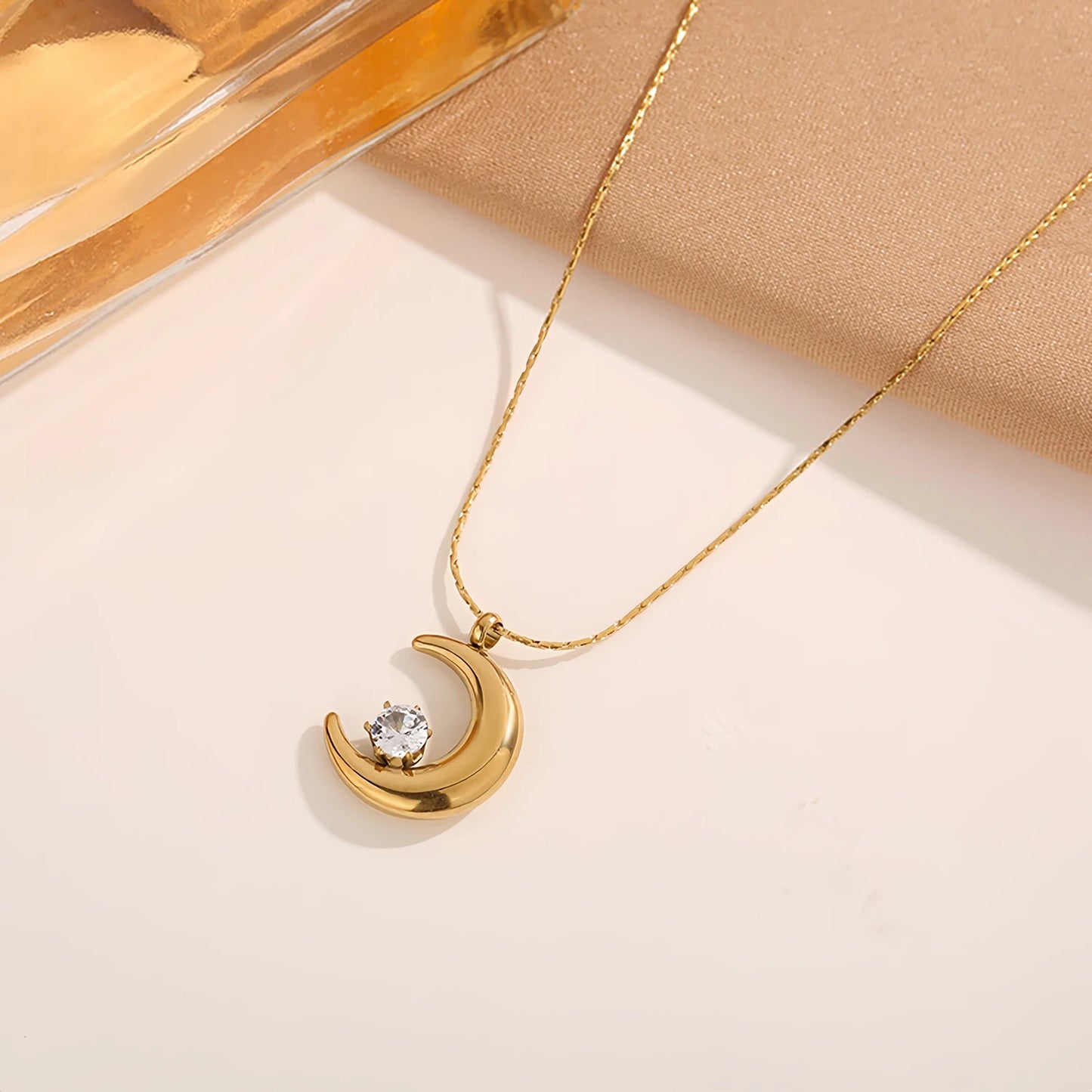 Gold necklace with a crescent moon pendant on a beige background