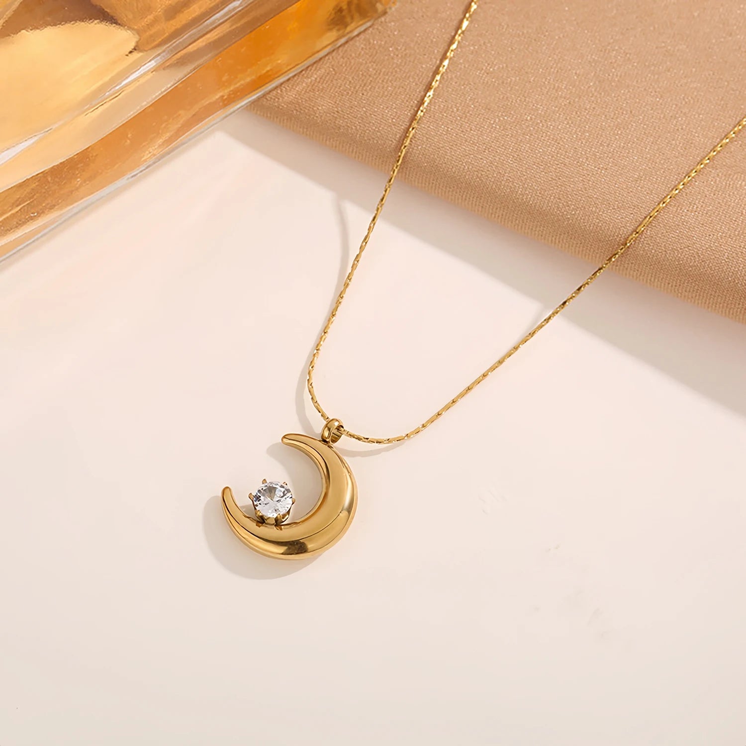 Gold necklace with a crescent moon pendant on a beige background