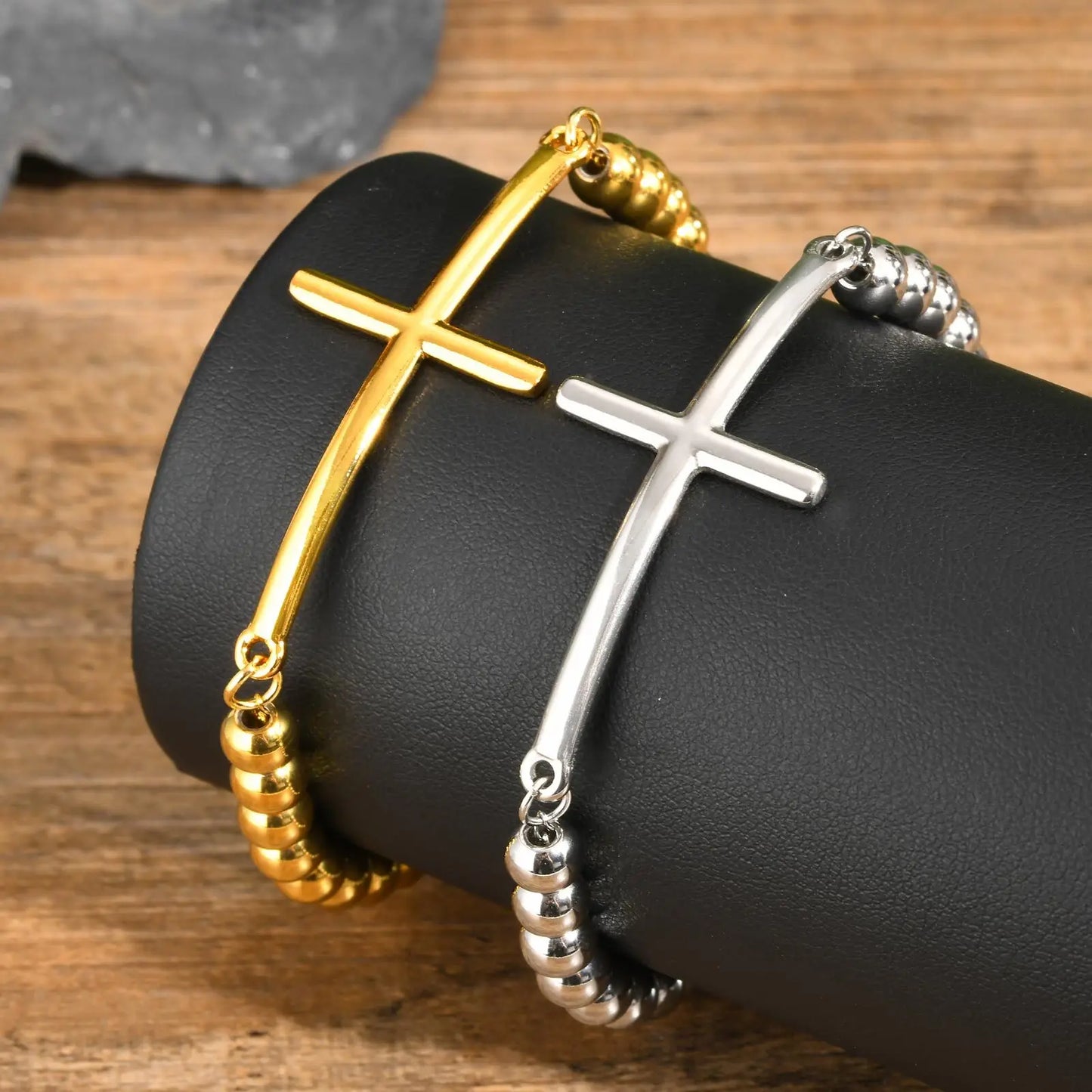 Gold and silver cross bracelets on a black leather surface with a wooden background