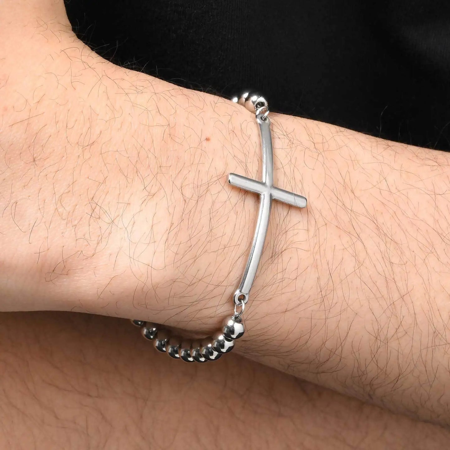 Silver bracelet with a cross on a wrist against a black background