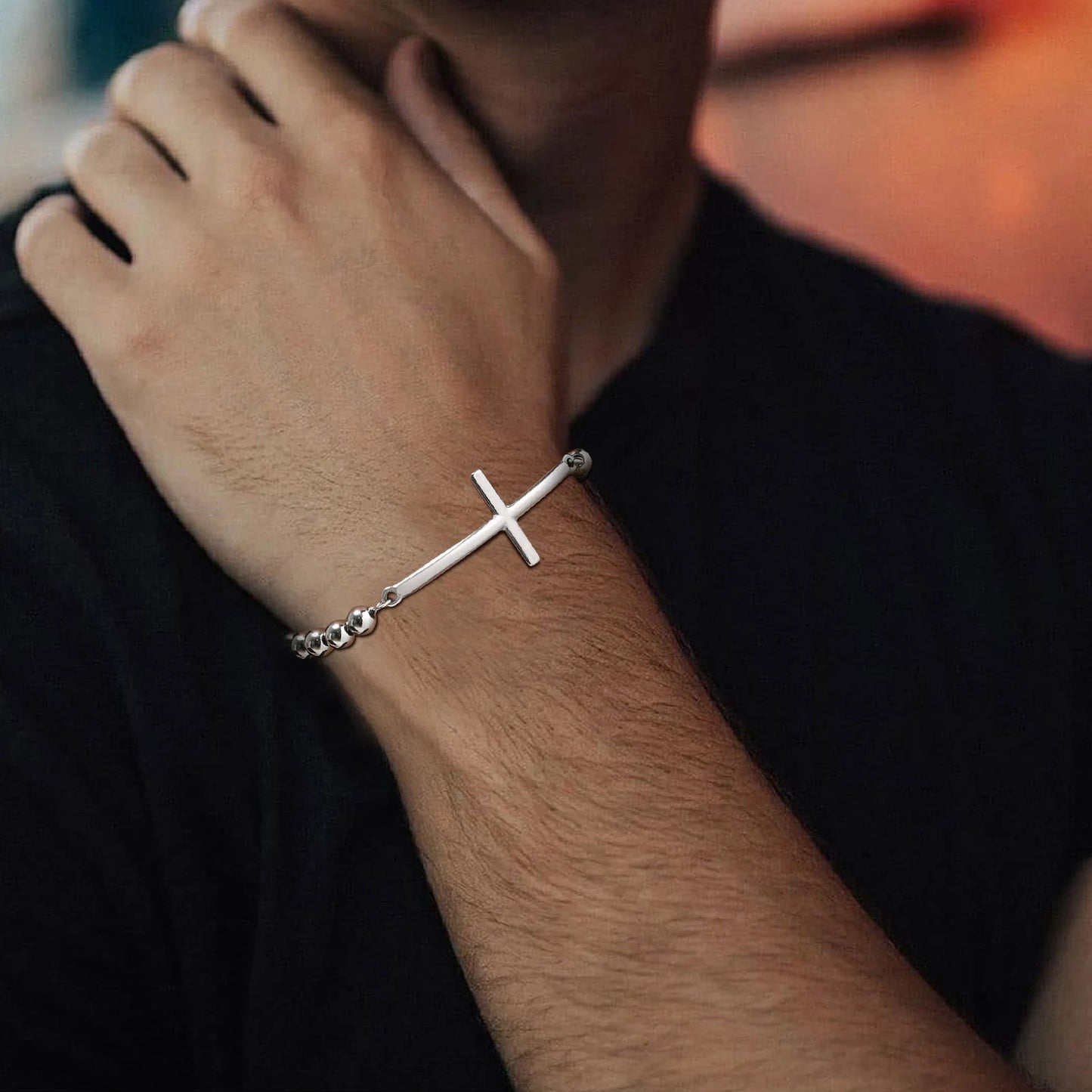Silver cross bracelet on a person's wrist with a blurred background