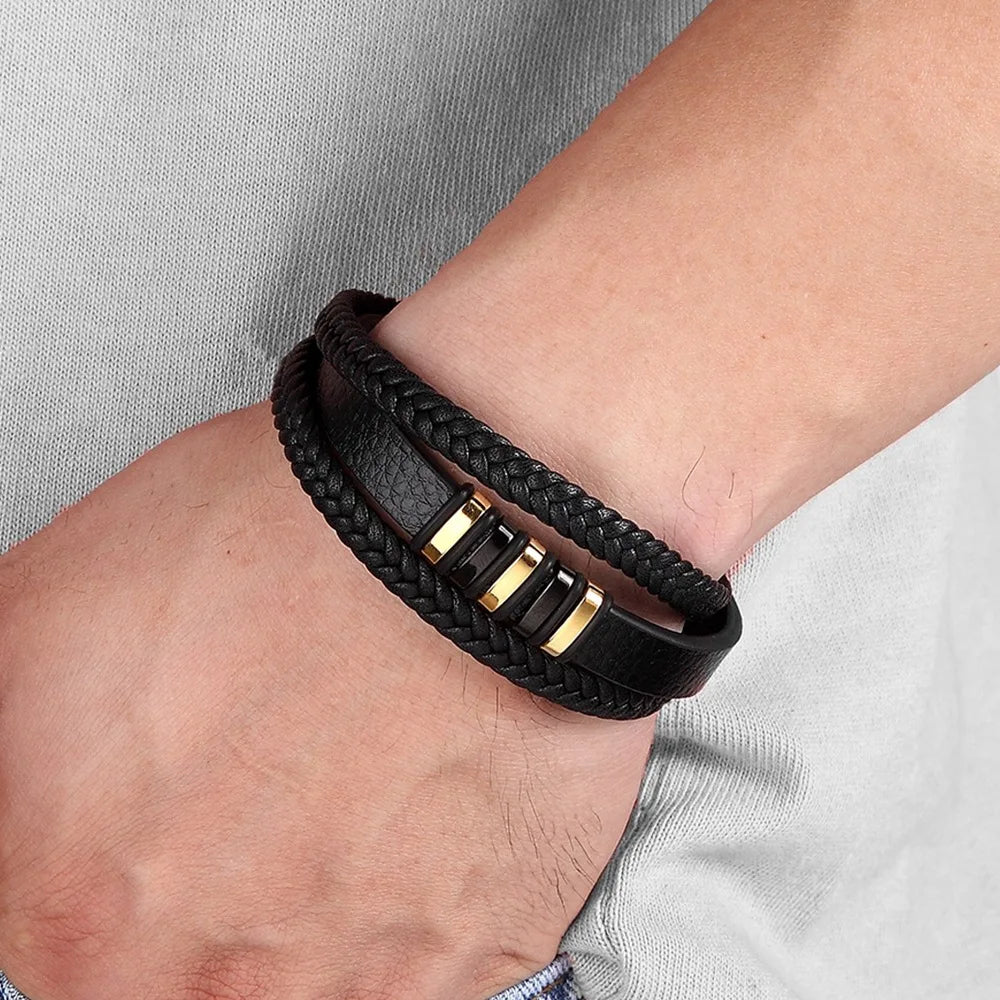 Black braided leather bracelet with gold accents on a wrist against a light gray background