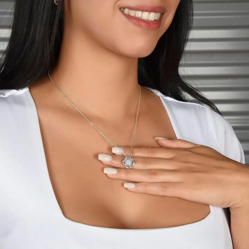 Woman wearing a silver necklace and holding a matching ring, against a neutral background