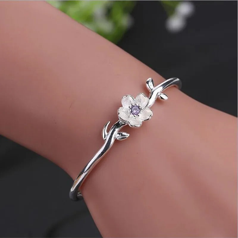 Silver bracelet with floral design on a wrist against a dark background