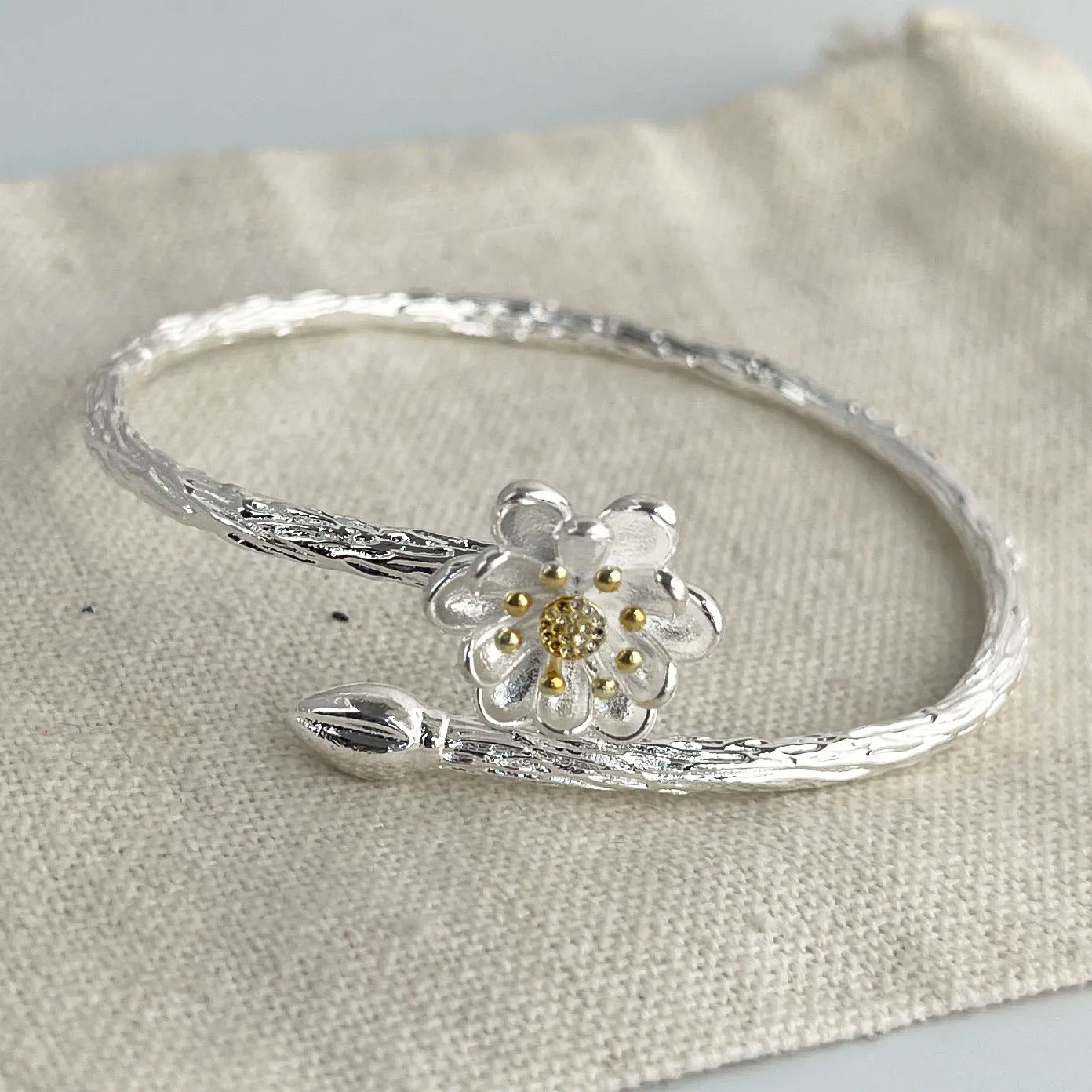 Silver bracelet with a floral design on a beige fabric background