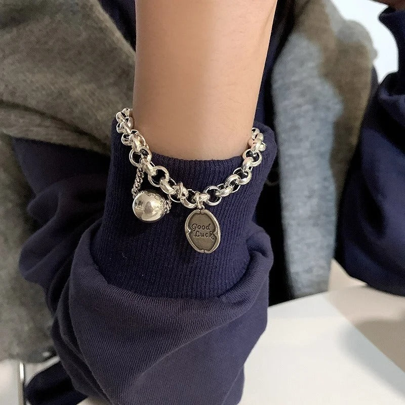 Person wearing a silver bracelet with charms on a navy sleeve.