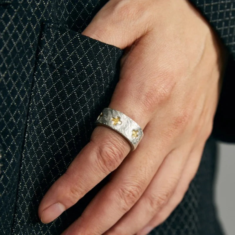 Hand wearing a silver ring with gold crosses on a textured fabric background