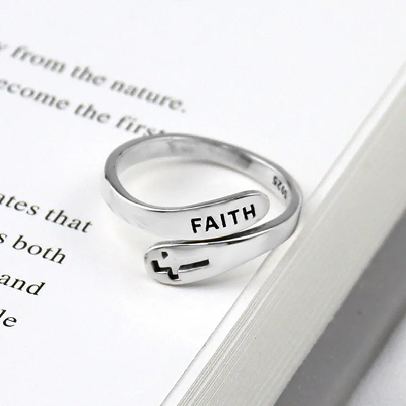 Silver ring with 'FAITH' engraved on it, placed on an open book.