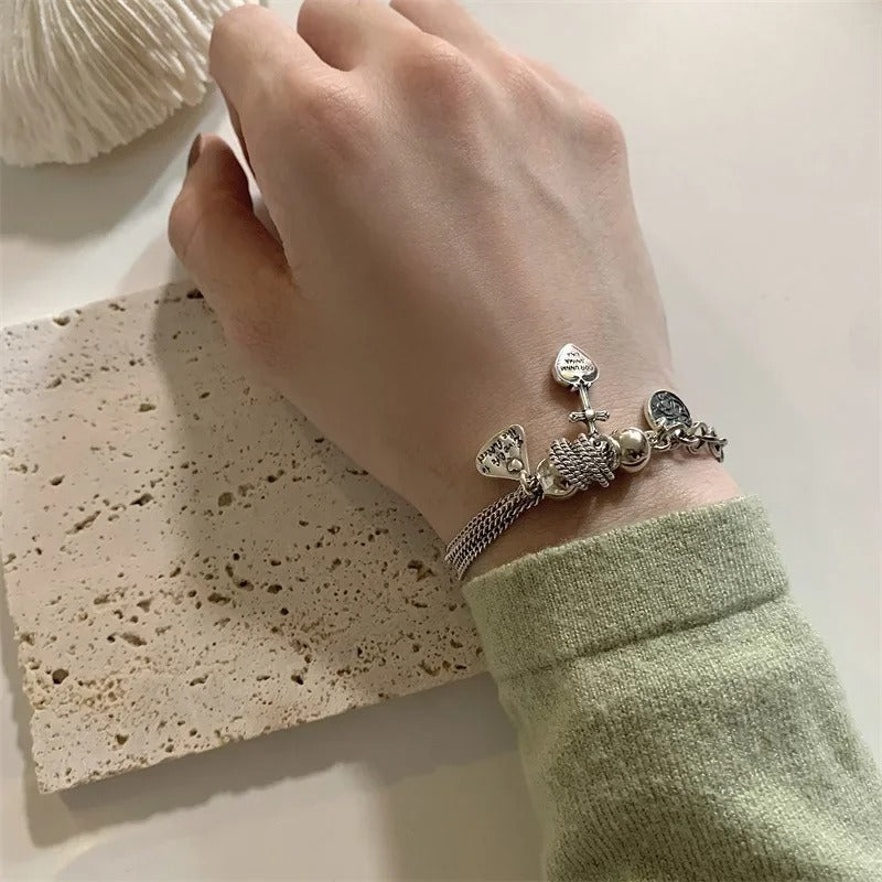 Hand wearing a silver bracelet with charms on a textured surface