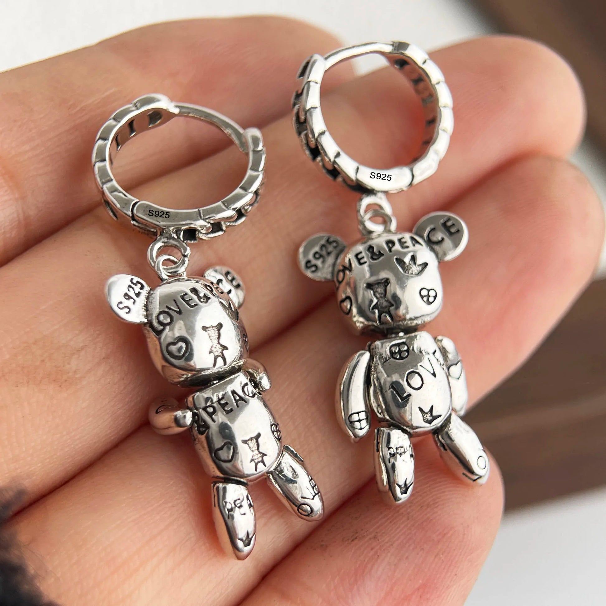 Silver teddy bear keychains with 'Love & Peace' text on a hand.