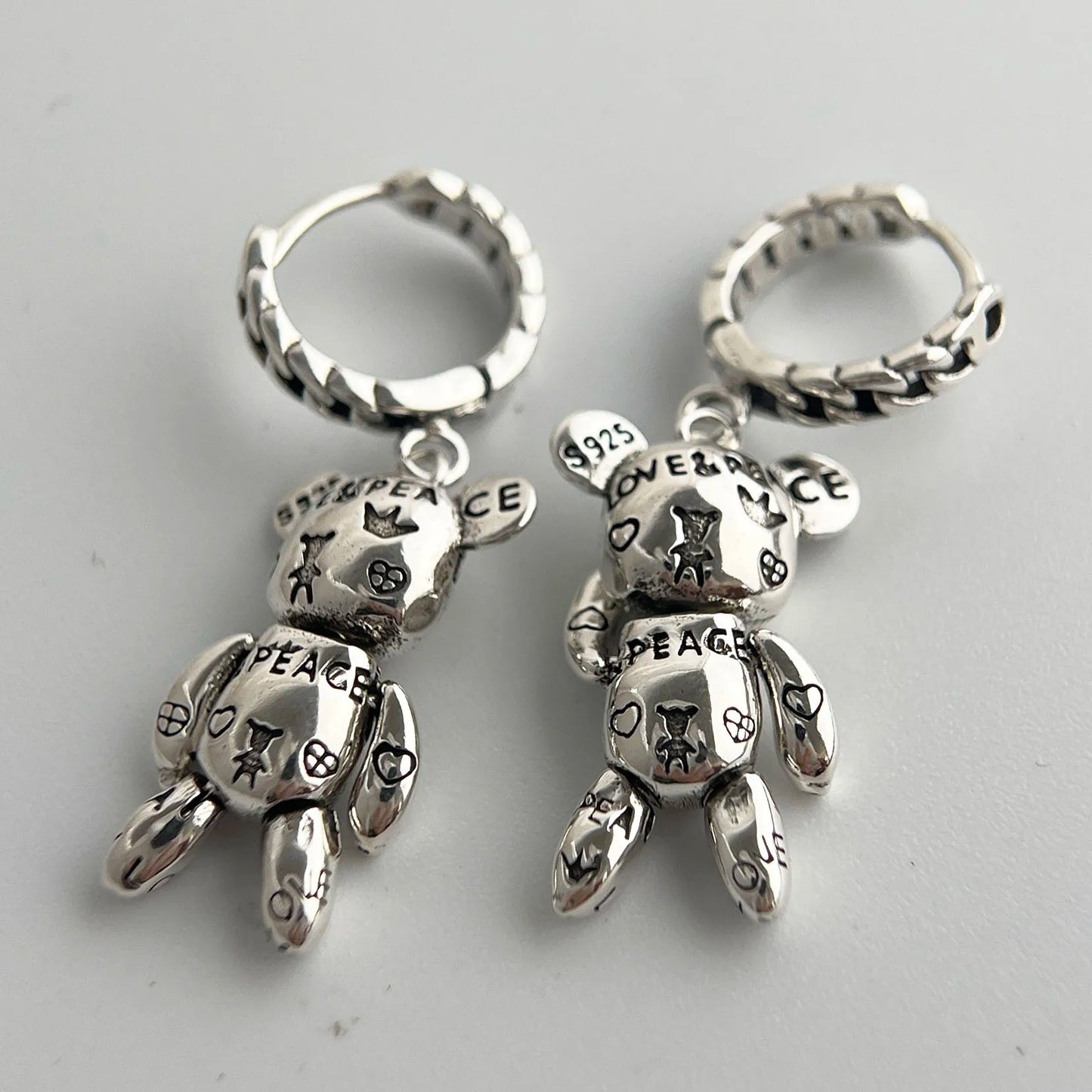 Silver teddy bear-shaped earrings with engraved text on a light gray background