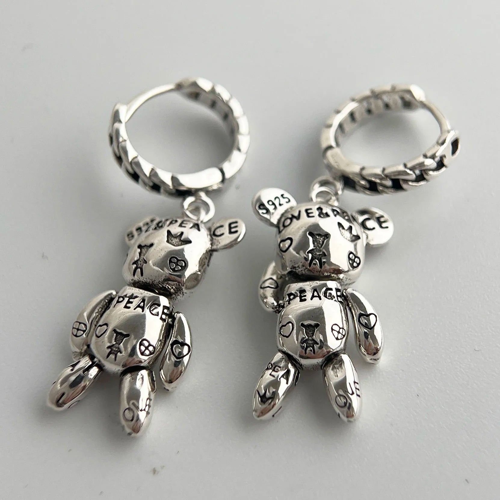 Silver teddy bear-shaped earrings with engraved text on a light gray background