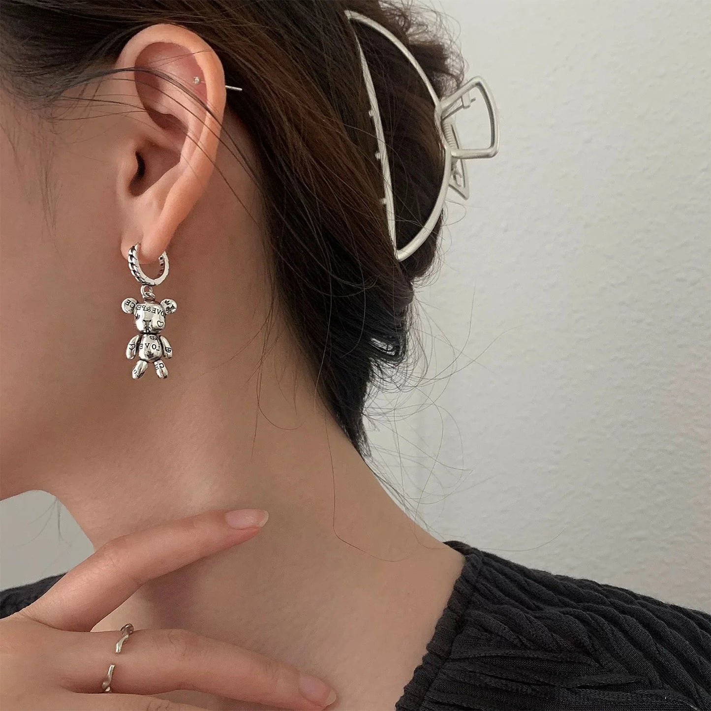 Close-up of a person wearing a silver bear-shaped earring with a neutral background