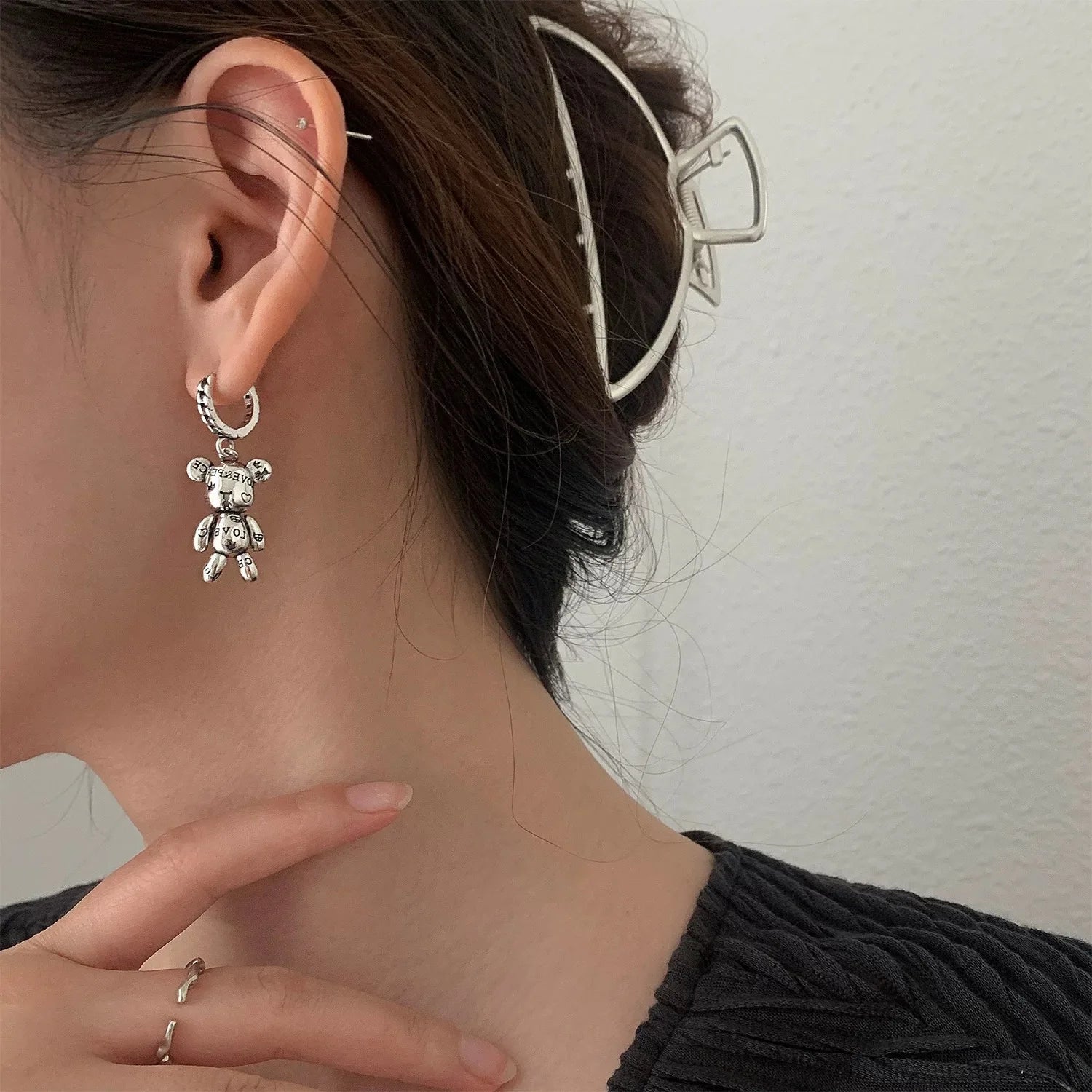 Close-up of a person wearing a silver bear-shaped earring with a neutral background