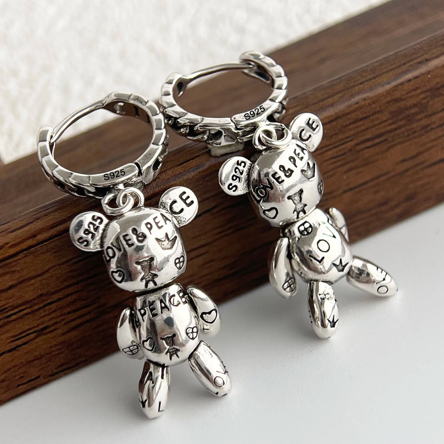 Silver teddy bear keychains with 'LOVE & PEACE' text on a wooden surface.