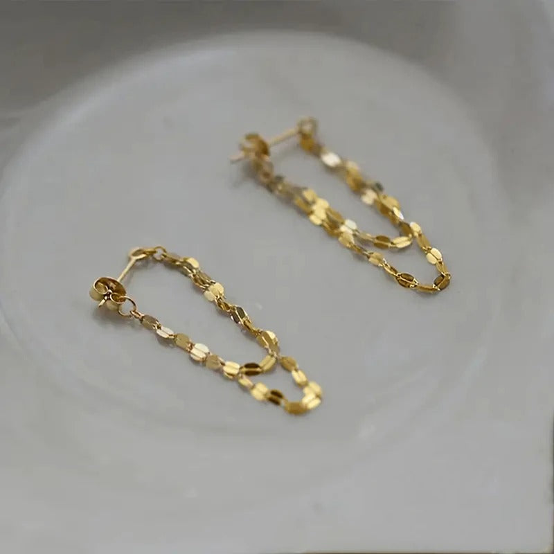 Gold chain earrings on a light gray background