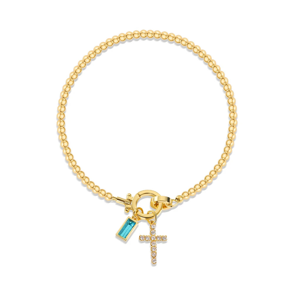 Gold bracelet with a blue charm and cross on a white background