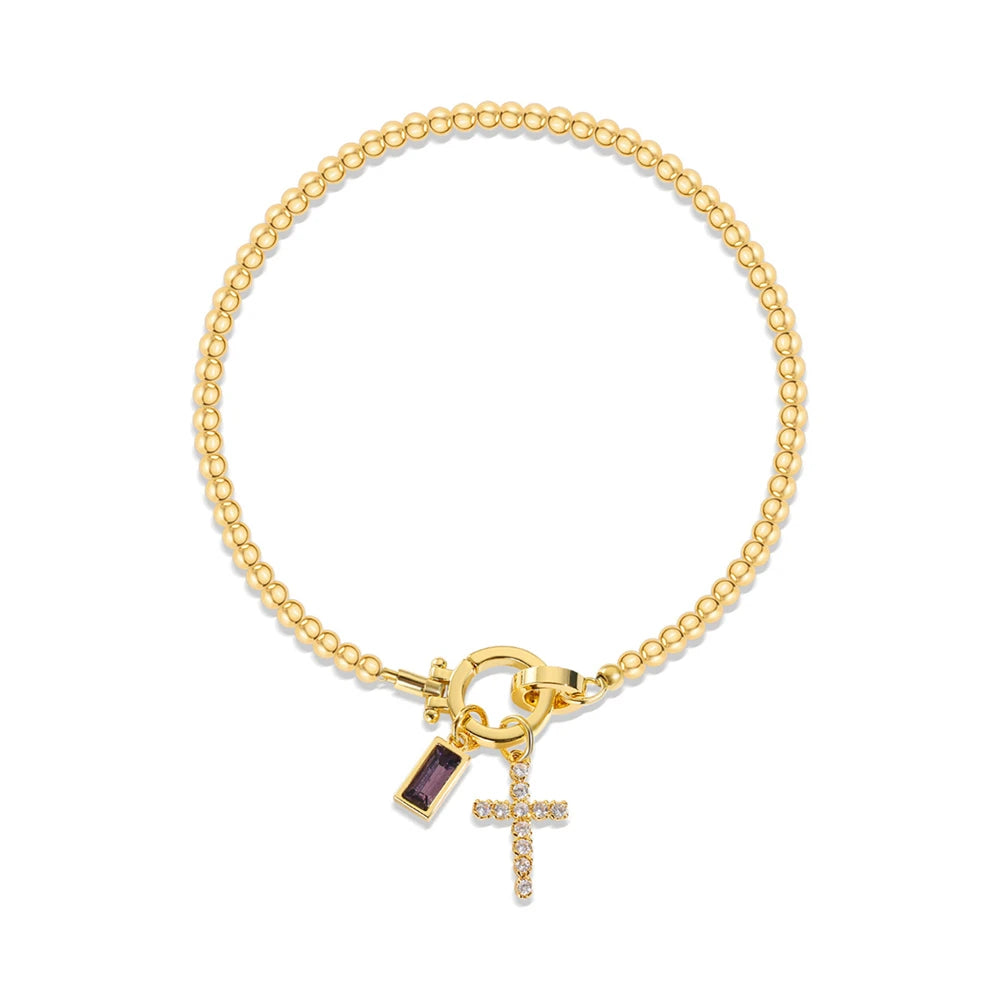 Gold bracelet with a cross charm and purple gemstone on a white background