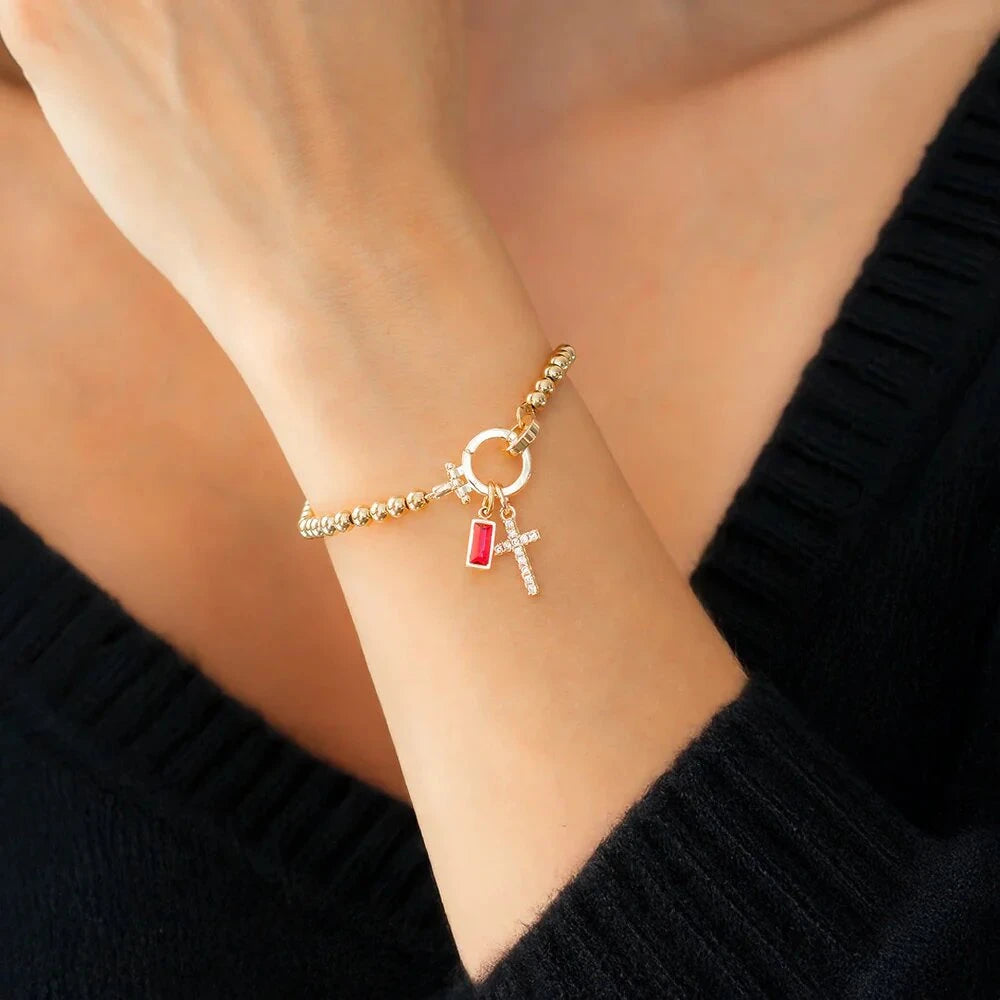Gold bracelet with charms on a wrist against a black sweater background