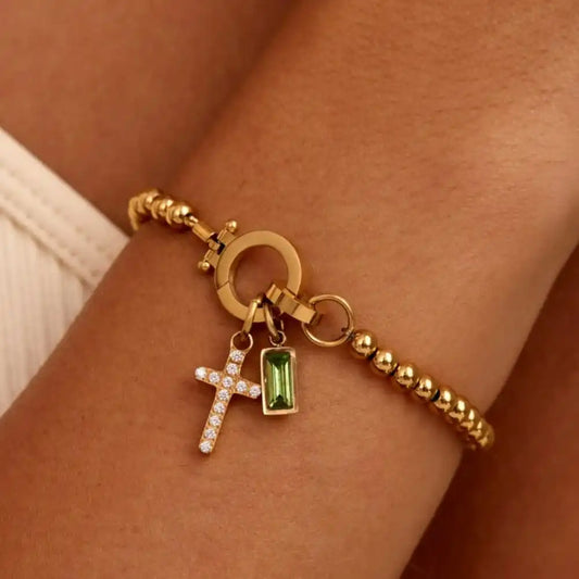 Gold bracelet with charms on a wrist against a neutral background