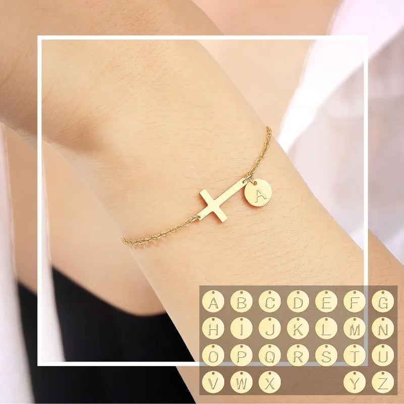 Gold bracelet with a cross and letter 'A' charm on a wrist, with a inset of additional charms.