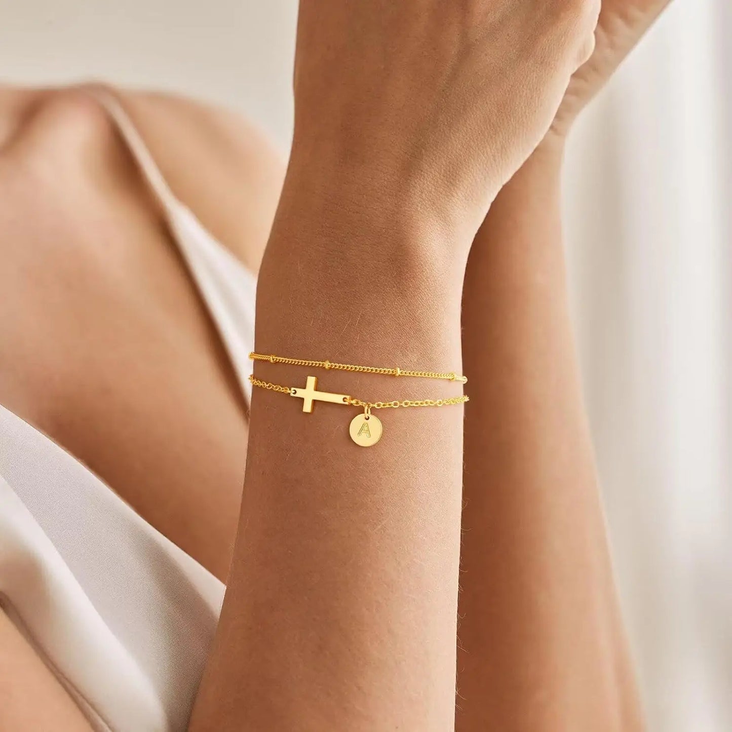 Gold bracelet with a cross charm on a wrist against a neutral background
