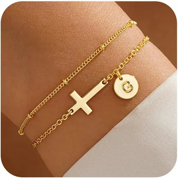 Gold bracelet with cross and circular charm on a skin-toned surface