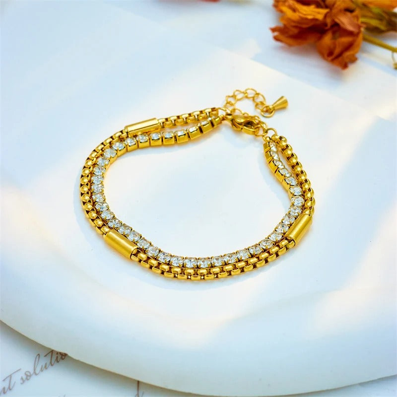 Gold bracelet with clear stones on a white surface with dried flowers.