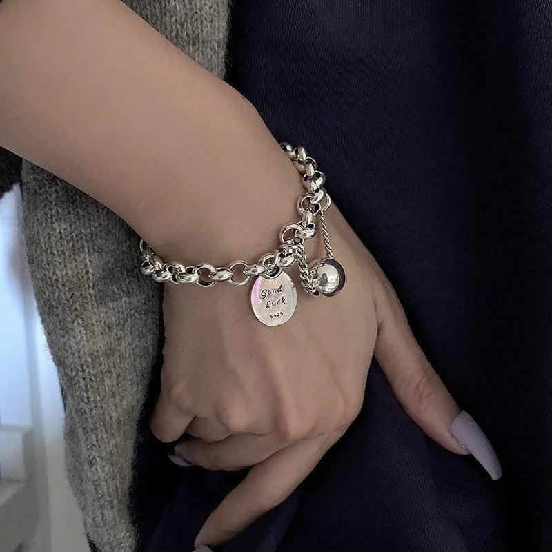 Hand wearing a silver bracelet with charms against a dark background