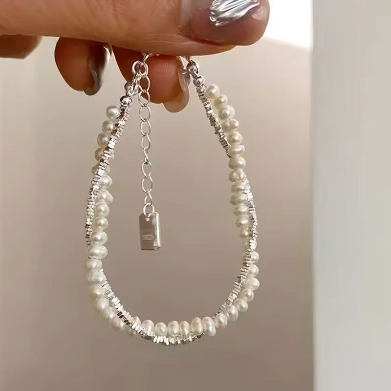 Pearl bracelet with silver chain held by a hand against a neutral background