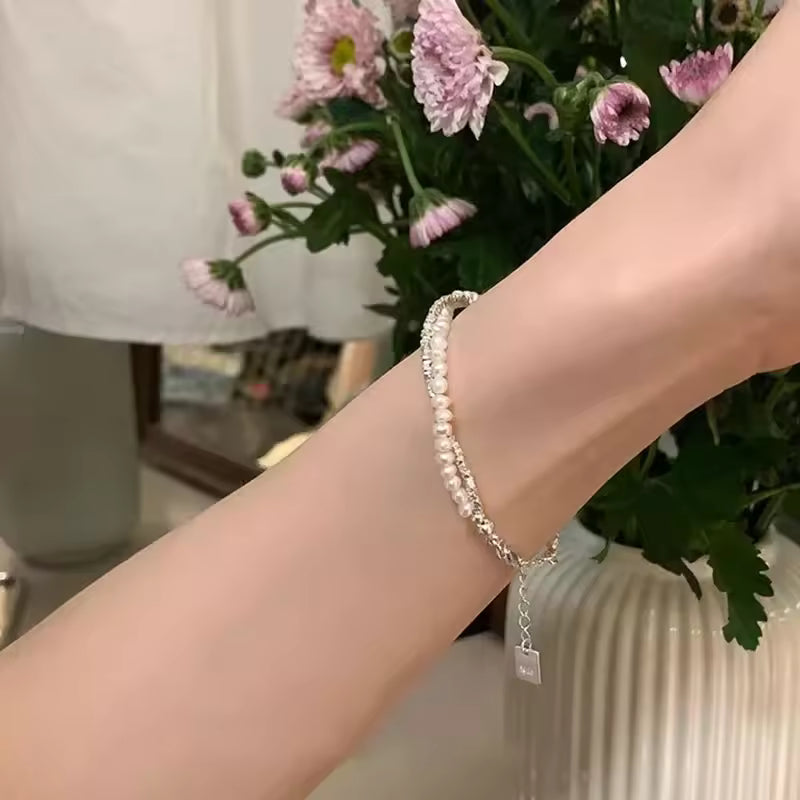 Close-up of a wrist wearing a pearl bracelet with a blurred background of flowers and a lamp.