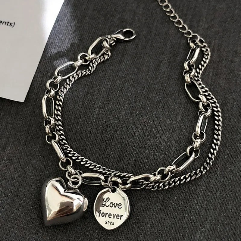 Silver chain bracelet with heart and 'Love Forever' charm on a dark surface