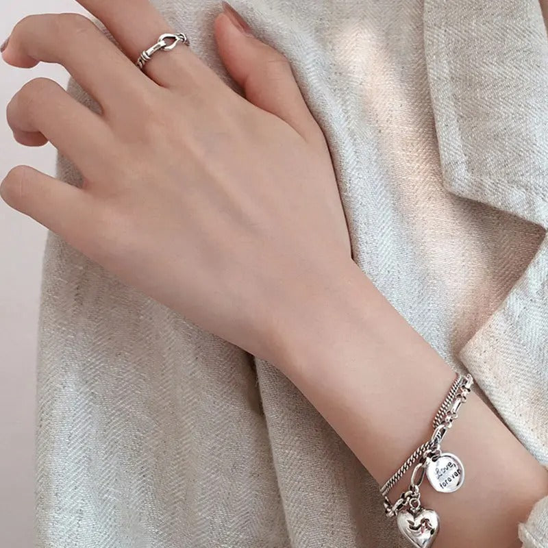 Hand wearing a silver bracelet with heart charms on a textured fabric background