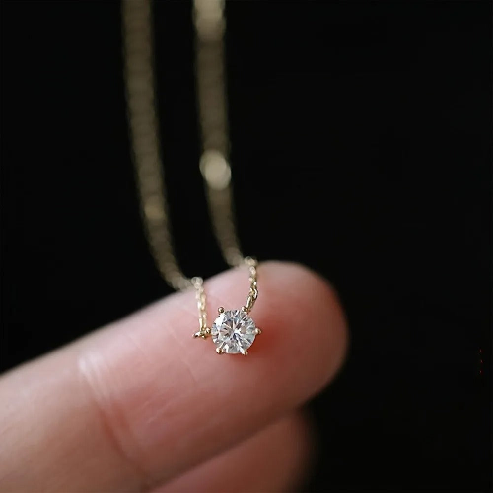 Gold necklace with a diamond pendant held between fingers against a dark background