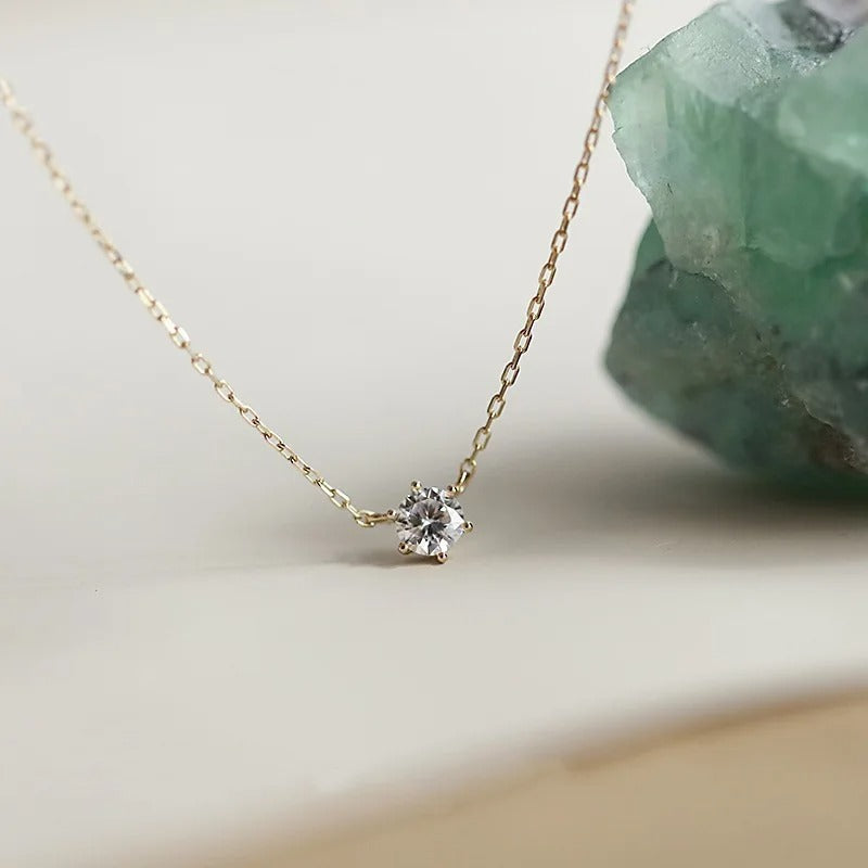 Gold necklace with a diamond pendant against a green crystal background