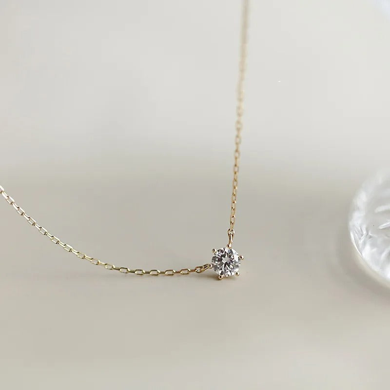 Gold necklace with a small diamond pendant on a light background