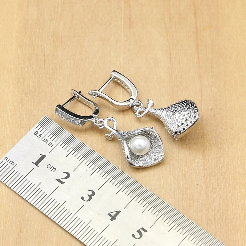 Silver earrings with a pearl on a wooden surface with a ruler for scale.