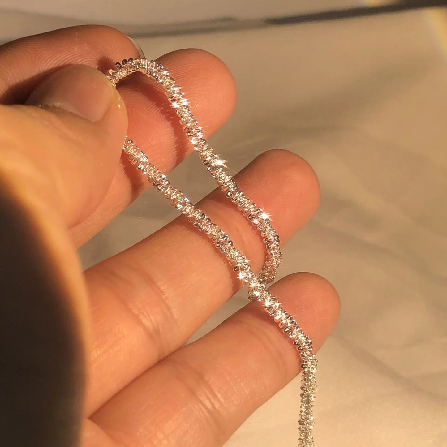 Silver bracelet held between fingers against a neutral background