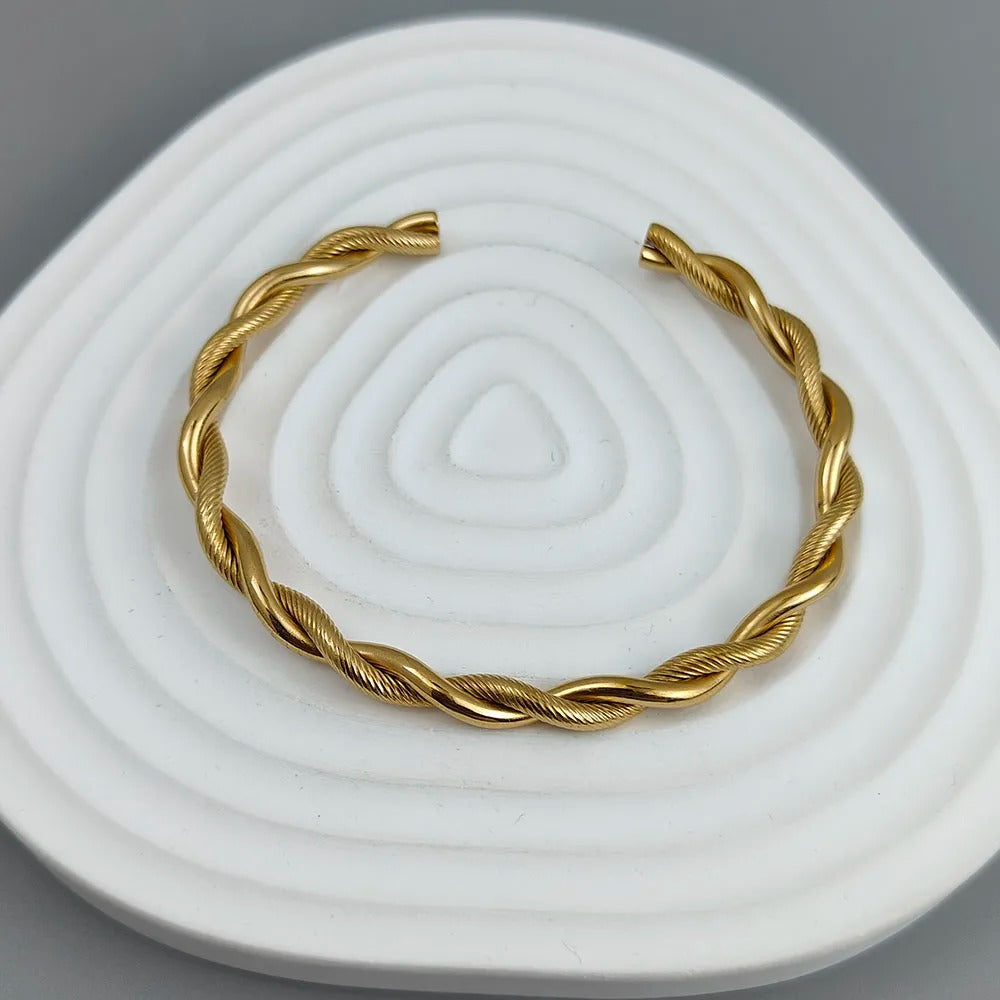 Gold braided bracelet on a white and gray textured surface