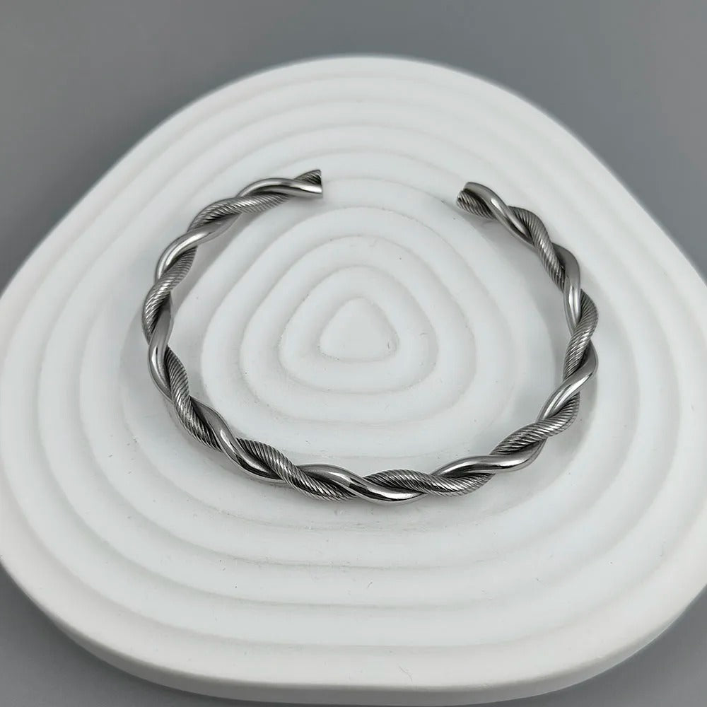 Silver twisted bracelet on a white stone surface with a gray background